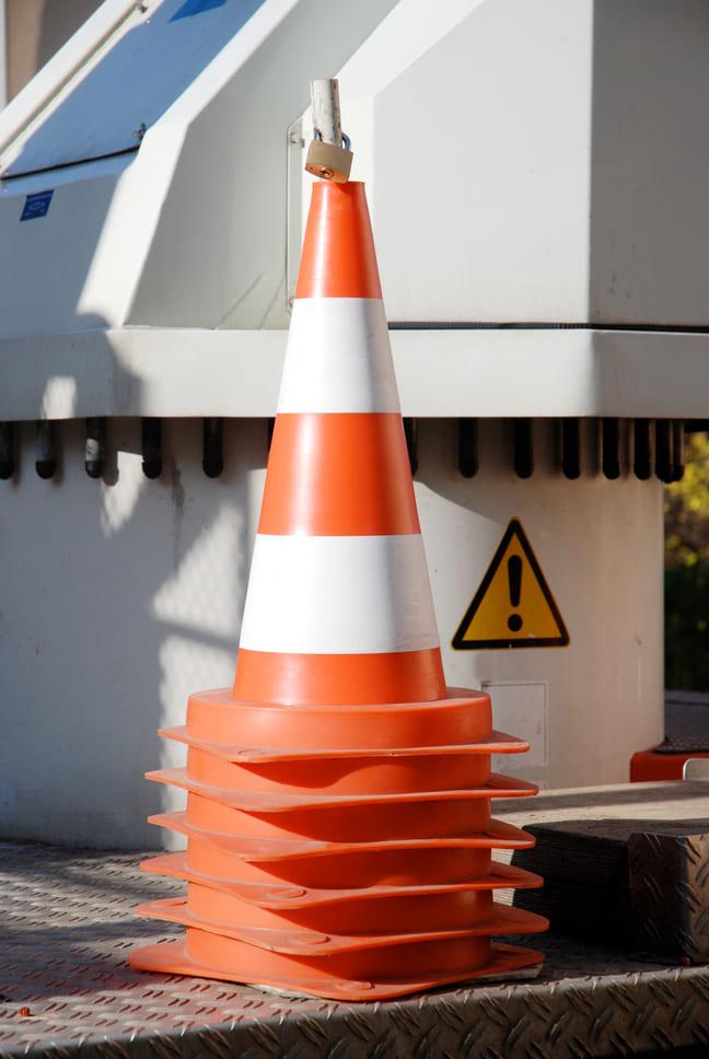 Verkehrsleitkegel vor einer Maschine mit einem Warnzeichen, das auf mögliche Gefahren hinweist, um die Sicherheit am Arbeitsplatz zu gewährleisten.