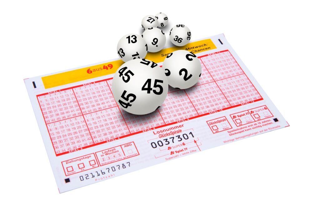 in ausgefüllter Lottoschein für das Spiel "6 aus 49" mit mehreren weißen Lottozahlenkugeln, die verschiedene Zahlen zeigen, darunter die Nummern 45, 13, und 2.